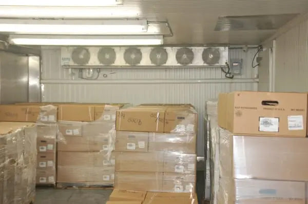 Commercial cold storage room with stacked pallets and a ceiling-mounted refrigeration evaporator system providing consistent cooling.