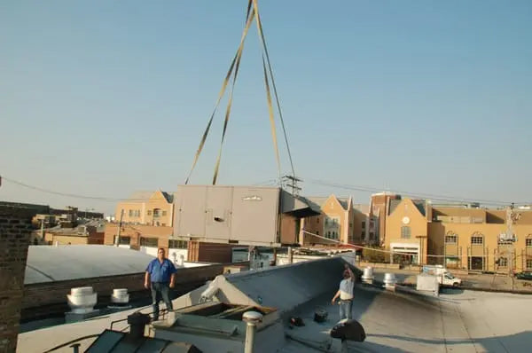 Rooftop commercial HVAC unit being crane-lifted into position by Temp-Master technicians during installation.