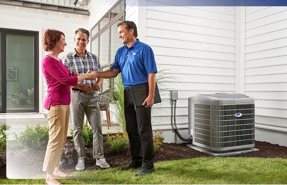 Two people shaking hands with a technician outside a house with an air conditioning unit.